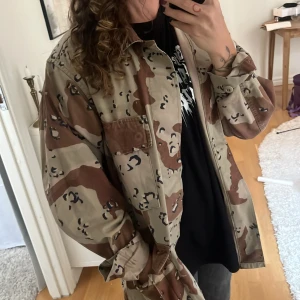 Camouflage overshirt desert style - Säljer en oversized desert camo overshirt med stora fickor framtill och klassisk krage. Jackan är i beige och bruna toner med svart camouflagemönster. Materialet är en mix av bomull och nylon, perfekt för dig som gillar militärinspirerad streetstyle.