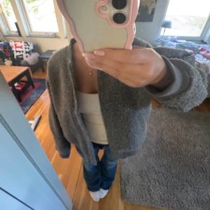 Teddy jacka  - Mysig grå teddyjacka i bombermodell med ribbade muddar och dragkedja framtill. Jackan har långa ärmar och coola dragkedjedetaljer på ärmarna. Perfekt för dig som gillar en chill och oversized vibe.