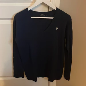 Mörkblå v-ringad tröja Polo Ralph Lauren - Klassisk mörkblå v-ringad tröja från Polo Ralph Lauren med broderad logga på bröstet. Tröjan har lång ärm och är i ett mjukt, stickat material som passar perfekt till lager-på-lager. Enkel och stilren design som funkar till allt. Priset kan diskuteras vid snabb affär.