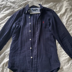Polo Ralph Lauren skjorta - Mörkblå skjorta från Polo Ralph Lauren med klassisk krage. Skick 9/10 änvänd under sommaren. Lite liten i storleken.