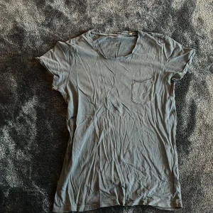 Grå t-shirt från Contemporary, M - En basic grå t-shirt från Contemporary i storlek M. T-shirten har rund halsringning, korta ärmar och en liten bröstficka. Tillverkad i mjuk bomull som känns skön mot huden. Perfekt till jeans eller shorts för en chill look.