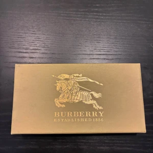 Burberry plånbok  - Säljer en snygg plånbok från Burberry med klassiskt rutigt mönster i beige, svart, vitt och rött. Aldrig använd