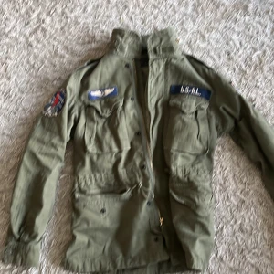 Grön militärinspirerad jacka Polo Ralph Lauren - Säljer en grön militärinspirerad jacka från Polo Ralph Lauren med coola patches och broderade detaljer. Jackan har flera fickor framtill, dragkedja och snörning i midjan. Perfekt för dig som gillar utility-stil och streetwear. helt ny. ny pris 5000kr