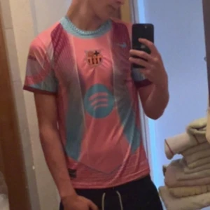 Barça x Spotify rosa/blå fotbollströja - Säljer en unik FC Barcelona fotbollströja från Nike i rosa och ljusblått med klubbmärke och Spotify-logga på bröstet. Tröjan är kortärmad och har ett modernt grafiskt mönster. Perfekt för dig som vill sticka ut på planen eller på läktaren.