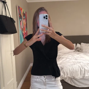 Svart omlottopp från Zara - Säljer en svart omlottopp från Zara med v-ringning och knyt i sidan. Toppen har korta ärmar och en stilren, figurnära passform. Perfekt att styla med både jeans och kjol för en snygg look.😍😍