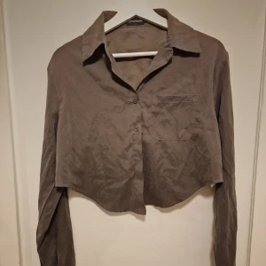 Croppad skjorta PrettyLittleThing - En grå/grön croppad skjorta som är snygg till jeans. Ger en cool avslappnad vibe. Ytters sparsamt använd.