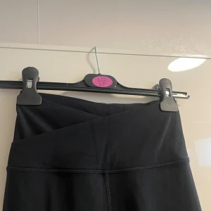 Svarta leggings från Glowmode XS - Svarta leggings från Gymshark i storlek XS med hög midja och snygg omlott-detalj framtill. Tillverkade i stretchigt material av polyamid och elastan för en tight och bekväm passform. Perfekta för träning eller chill dagar.