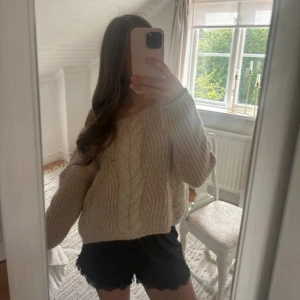 Beige stickad offshoulder tröja - Supermysig beige stickad tröja med grova flätmönster och offshoulder-passform. Tröjan är lite oversized och har långa ärmar, perfekt för lager på lager under kyliga dagar. Snygg att styla med både jeans och kjol.