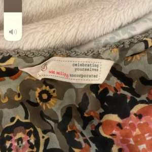 Blommig blus från Odd Molly - Säljer en blommig blus från Odd Molly med korta puffärmar och v-ringning. Blusen har ett färgstarkt mönster i orange, rosa, svart och beige på en grön bakgrund. Materialet är lätt och luftigt, perfekt för vår och sommar. Snygga rynkade detaljer framtill.