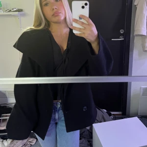 Svart jacka - Säljer en svart skepparkavaj med bred krage och dubbelknäppning framtill. Jackan har en loose passform och är tillverkad i ullmaterial, vilket gör den både snygg och varm. Perfekt att styla med jeans och boots för en cool look.#stockhomstil