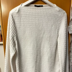 Vit långärmad stickad tröja - Säljer en vit långärmad stickad tröja från ISLE. Tröjan har ett snyggt strukturerat mönster och rak passform. Perfekt att matcha med jeans eller kjol för en clean look.