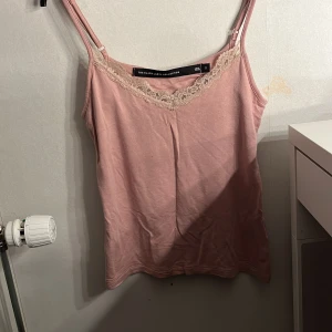 Rosa linnetopp med spets från 157 - Säljer en ljusrosa linnetopp från 157 med justerbara smala axelband och v-ringning dekorerad med beige spets. Toppen är i mjuk bomull och har en enkel, feminin look som passar perfekt till sommaren och som mys linne. Aldrig använd!