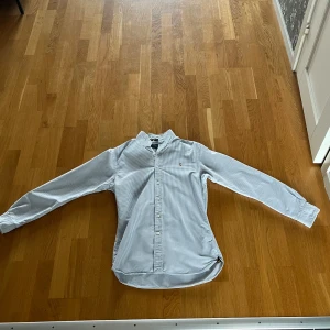 Randig skjorta Polo Ralph Lauren S - Säljer en slim fit skjorta från Polo Ralph Lauren i storlek S. Skjortan är vit med tunna blå ränder, har klassisk krage, långa ärmar och knäppning framtill. Tillverkad i bomull och har den ikoniska broderade loggan på bröstet.