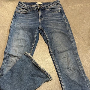 Blå bootcut jeans från Gina Tricot - Snygga blå jeans från Gina Tricot i bootcut-modell med råa, fransiga benslut. Klassisk femficksdesign och normal passform. Jeansen är tillverkade i denim med lätt tvättad look och har knapp- och dragkedjestängning.
