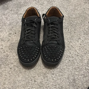 Svarta Louboutin!REPLIKAS! - Svarta sneakers i mocka från Christian Louboutin med ikonisk röd sula och svarta nitar på tån. Skorna är repliker men är ändå jätte snygga. den är pytte pytte lite sönder där man ska ta på skorna men inget man märker