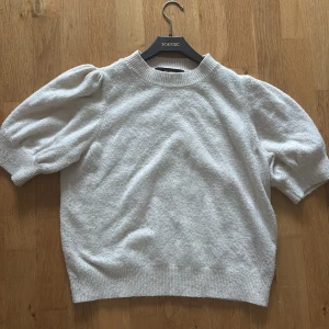 Ljusrosa/beige  stickad T-shirt med puffärm - Superfin ljusrosa/beige stickad tröja med korta puffärmar och ribbade muddar vid hals, ärmslut och nederkant. Perfekt för dig som gillar en enkel men ändå trendig look. Mjuk och skön, passar till både jeans och kjol.