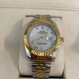 Datejust silver/guld herrklocka - Säljer en klassisk Datejust med silverfärgad urtavla, romerska siffror och datumfönster. Klockan har tvåfärgad länk i stål och guld samt räfflad guldfärgad ring runt urtavlan. En riktigt ikonisk accessoar med exklusiv känsla och tidlös design.