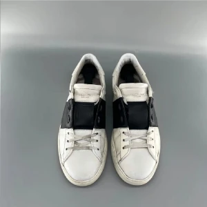 Valentino Garavani Open sneakers svart/vit - Snygga Valentino Garavani Open sneakers i vitt skinn med bred svart läderdetalj över vristen. Klassisk låg modell med snörning och ikoniska nitar baktill på sulan. Perfekta för dig som gillar stilrena och exklusiva sneakers med edge.