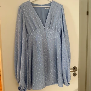 Adoore- Florence dress - Supersöt ljusblå klänning från Adoore med små vita blommor, v-ringad hals och långa puffärmar. Klänningen har knappar framtill. Hör av dig vid intresse🌟🌸🙌🏼