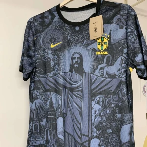 Brasil Nike svart/blå fotbollströja - Snygg Brasilien fotbollströja från Nike i svart och mörkblått med unikt grafiskt mönster över hela framsidan, inklusive Kristusstatyn och brasilianska motiv. Gult Brasil-märke och Nike-logga på bröstet. Tillverkad i lätt, andningsbart material med Dri-FIT-teknologi. Rund hals och korta ärmar.