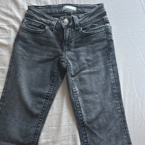 Grå bootcut jeans från Gina Tricot - Snygga grå jeans från Gina Tricot med bootcut-modell och klassisk femficksdesign. Jeansen har markerade sömmar, silverfärgade knappar och bakfickor med lock. Perfekta för dig som gillar en retro vibe och vill ha ett par jeans med lite utsvängda ben.