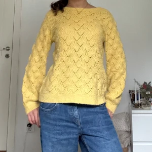 Gul stickad tröja med mönster - Superfin gul stickad tröja med ett snyggt hålmönster över hela. Tröjan har rund halsringning och långa ärmar med ribbade muddar. Perfekt för dig som vill ha en färgklick i garderoben!