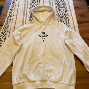 Vit hoodie med japanskt tryck från YOURTURN - Säljer en vit hoodie från YOURTURN med japansk text och coolt tryck av Shibuya på ryggen. Hoodien har huva med snörning, känguruficka och mjukt material. Perfekt för dig som gillar streetstyle och unika detaljer. 