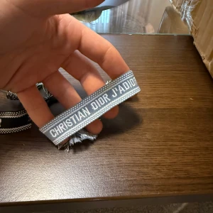 Ljusblå Christian Dior J'Adior armband - Snyggt grått armband från Christian Dior med texten 'J'Adior' broderad i vitt.
