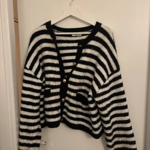 Randig fluffig kofta med guldknappar - Supermysig svartvit randig kofta från Gina tricot  med  snygga guldknappar framtill. Koftan har två små fickor och lång ärm, perfekt för lager på lager under kyliga dagar.