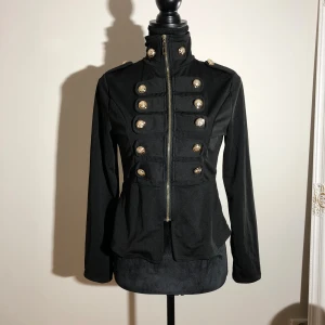 Svart rock med guldknappar från Qiaomeng - Längd ca 60cm. Ärmlängd ca 60cm. Pris: 10kr 