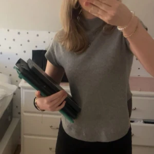 Topp från Wera i ull - Säljer en enkel och snygg grå ull topp från Wera. Toppen har en rak passform, korta ärmar och rund halsringning. Perfekt att matcha med jeans eller kjol för en clean look. Har använt max 3 gånger. Orginalpris 599kr