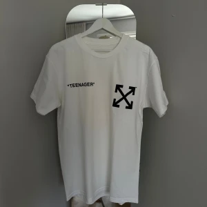 Off-White x Simpsons “Teenager” T-shirt – Vit, strl L - Oanvänd sällsynt t-shirt från Off-White med unikt Simpsons-samarbete. Framsidan har texten “TEENAGER” och den klassiska Off-White-loggan, medan baksidan pryds av ett stort tryck av Bart Simpson i eld med citatet “I’m Bart Simpson, who the hell are you?”. En statement-piece som blivit en riktig grail bland samlare.