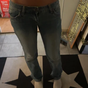 Blå Lågmidjade jeans med nitar och slitningar - Snygga blå jeans med slitningar och nitar på bakfickorna. Modellen har låg midja och raka ben med klassisk femficksdesign. Jeansen är tillverkade i denim och har coola detaljer. Dom är i storlek xs