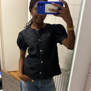 Mörkblå blus med puffärm och knappar - Säljer en mörkblå blus i denim-look med korta puffärmar och silverfärgade knappar framtill. Använt endast 3 gånger🌸 storlek M men passar mig fint som bär S vanligtvis!