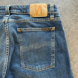 Nudie Jeans Skinny Lin - Snygga blå jeans från Nudie Jeans med klassisk femficksdesign och orangea sömmar. Modellen är skinny med smal passform och normal midja. Materialet är mjukt denim i bomull och jeansen har en stilren look med Nudie-logga på bakfickan.