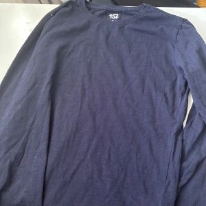 Mörkblå långärmad tröja från 157 - En basic mörkblå långärmad tröja från 157. Tröjan har rund halsringning och är tillverkad i mjuk bomull, perfekt för lager-på-lager eller som den är. Enkel och stilren design som funkar till det mesta.