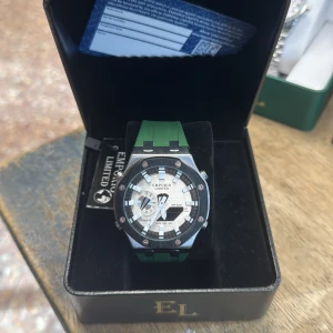 Grön och silver klocka Emporio Limited - Snygg klocka från Emporio Limited med grön silikonrem och robust boett i silverfärgad metall. Urtavlan är vit och svart med markerade index och flera funktioner, bland annat datumvisning. Kommer i lyxig svart ask med gulddetaljer.