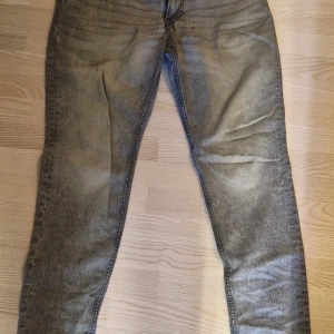 Grå tapered jeans från H&M 34/32 - Snygga grå jeans från H&M i modellen Tapered Regular Fit. Jeansen har en tvättad look, klassiska fem fickor och dragkedja. Passformen är smalare nertill för en modern siluett. Perfekta för dig som gillar en avslappnad men ändå stilren vibe.