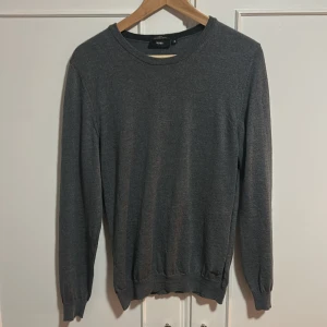 Mörkgrå merinoullströja från BOSS - Snygg mörkgrå rundhalsad tröja från BOSS i extrafin merinoull. Slim fit-modell med långa ärmar och ribbade muddar vid ärmslut och nederkant. Perfekt för dig som gillar stilrena och klassiska plagg med en modern passform.