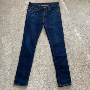 Nudie Jeans - Klassiska Nudie Jeans i mörkblå denim med snygg orange söm och perfekt passform. Slim fit-modell med normal midja och lagom stretch för en bekväm men stilren look. Nypris: 1600 - 1900 kr Modell: Lean Dean Storlek W33 L34.