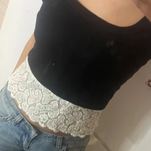 Vit spetsig linnetopp med blommönster - Superfin vit linnetopp med blommigt spetsmönster och tunna axelband. som sitter snyggt på kroppen och ger en romantisk vibe. Perfekt att styla med jeans eller kjol för en fräsch look. Passar jättebra att ha under andra tröjor