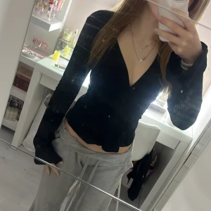 Svart omlottopp med knytband - Säljer en svart omlottopp med långa ärmar och djup v-ringning. Toppen har knytband i midjan som ger en snygg passform och är tillverkad i ett lätt, strukturerat tyg. Perfekt för dig som gillar stilrena och trendiga plagg.