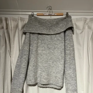 Grå offshoulder stickad tröja Gina Tricot - Supermysig grå stickad tröja från Gina Tricot med bred offshoulder-krage. Perfekt för kyliga dagar och har en avslappnad passform med långa ärmar och ribbade detaljer vid krage, ärmslut och nederkant.