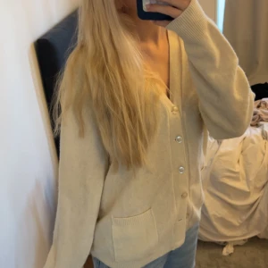 Beige kofta med fickor och knappar - Mysig oversized beige kofta med v-ringning och stora silvriga knappar framtill. Koftan har två praktiska fickor och ribbade muddar vid ärmslut och nederkant. Passar perfekt till jeans och har en loose fit som ger en chill vibe. Står ingen storlek, men skulle uppskatta till en M/L