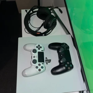 PlayStation 4 Pro White + 2 DualShock 4 + Headset - Snygg vit PlayStation 4 Pro med två DualShock 4-kontroller (svart och vit) samt ett gamingheadset. Konsolen och kontrollerna är i gott skick med mindre ytliga repor. Perfekt för spel och multiplayer direkt ur kartong. Priset är inte hugget i sten vid snabb affär.
