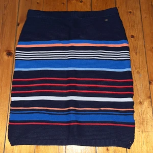 Randig kjol från Holly & Whyte - Snygg stickad kjol från Holly & Whyte med horisontella ränder i marinblått, blått, vitt, rött och orange. Kjolen har en elastisk midja och är gjord i mjukt stickat material som sitter bekvämt och har en cool, ungdomlig vibe.