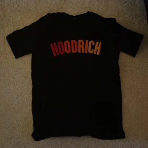 Svart HOODRICH t-shirt med färgglatt tryck - Svart t-shirt från HOODRICH med stort tryck i rött, orange och gult över bröstet. Klassisk rund hals och korta ärmar. T-shirten är gjord i mjuk bomull och har en clean look med fokus på det färgstarka logotyp-trycket framtill. Mindre passform.