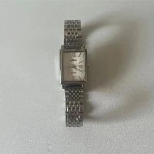 Silverfärgad klocka med länk - Stilren klocka med rektangulär urtavla och klassisk länkarmband i silverfärgat metall. Urtavlan har romerska siffror och en diskret design som passar till många olika stilar. Perfekt accessoar för dig som gillar tidlös look.