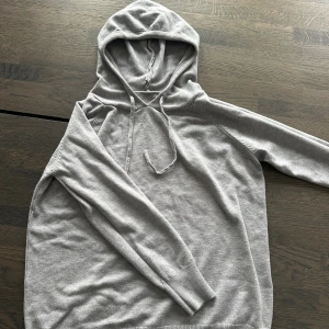 Merinoull hoodie - En stilren ljusgrå merinoull hoodie med huva och snörning framtill. Tröjan har långa ärmar och ribbade muddar vid ärmslut och nederkant. Perfekt för en chill och avslappnad look. Materialet känns mjukt och skönt mot huden.