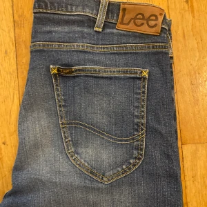 Blå Lee Luke jeans W36 L34 - Säljer ett par klassiska blå Lee Luke jeans med snygg tvätt och kontrastsömmar. Modellen har normal passform och raka ben, tillverkade i bomull med lite stretch för extra komfort. Ikonisk Lee-lapp bak i midjan och femficksdesign.